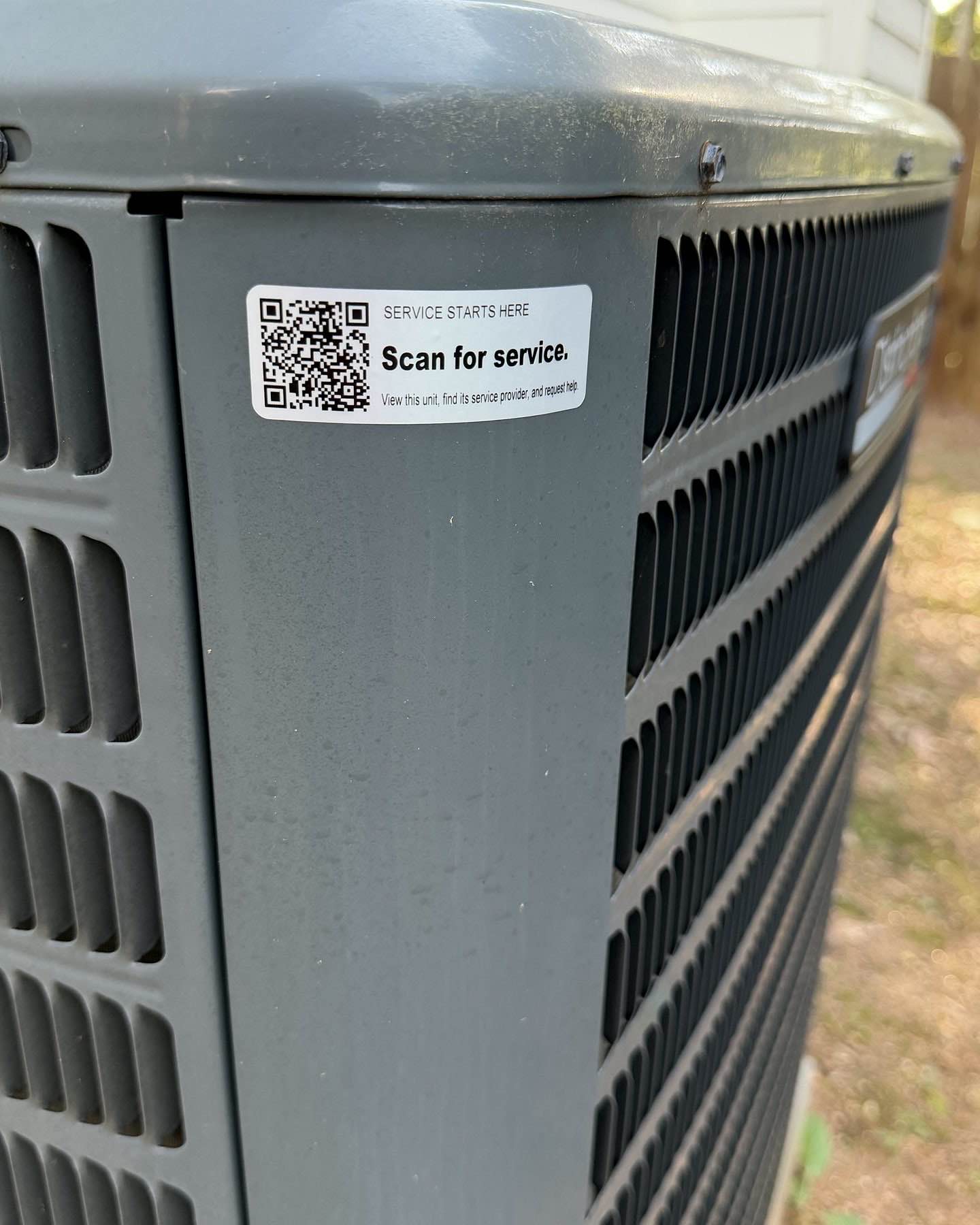 Close view of a Tech Was Here QR service tag installed on an outdoor HVAC condenser